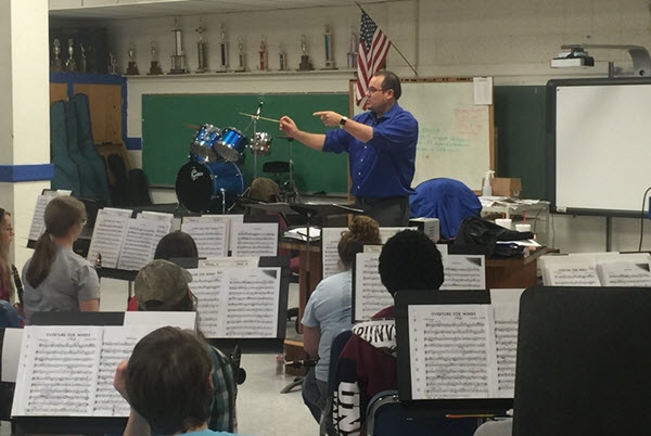 Dr. Miller Male teacher conducting a school band class of teenagers.