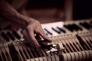 A piano craftsman adjusting a hammer on a key assembly.