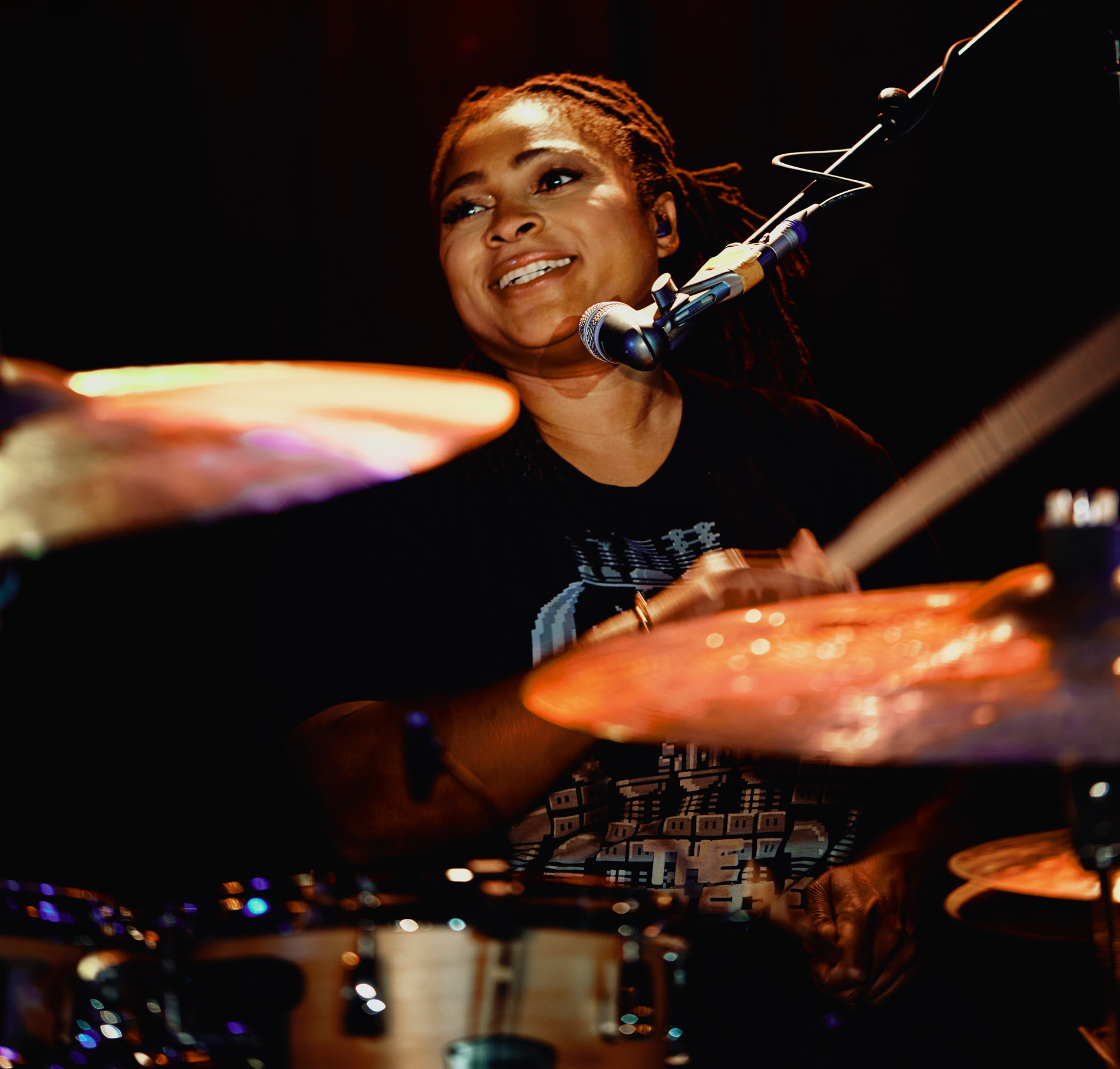 Nikkie-Glaspie-body-image-1-resize Woman smiling and playing drums.