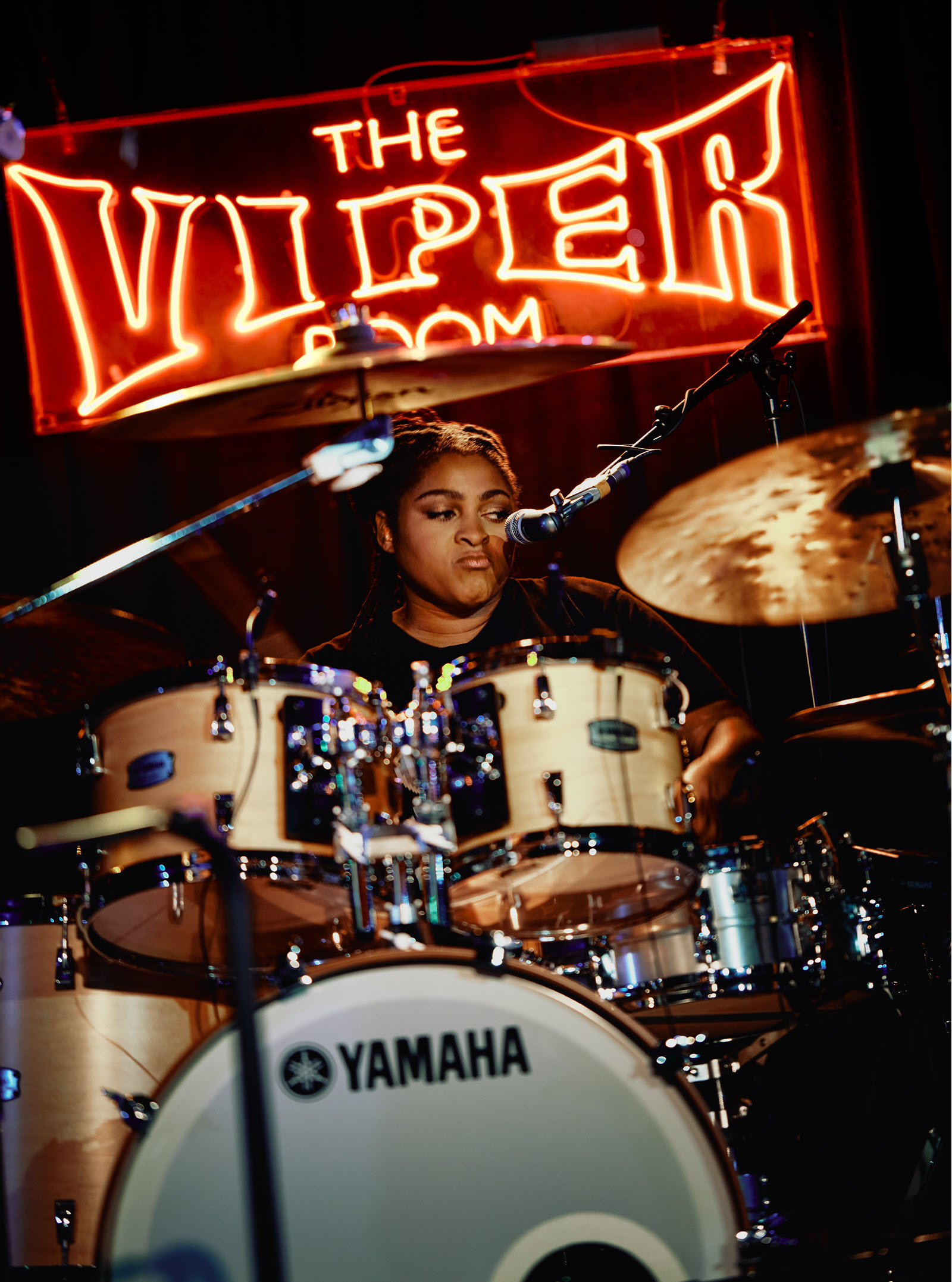 Nikkie-Glaspie-body-image-3-resize Woman playing drums with lit up sign behind her that says "The Viper Room".